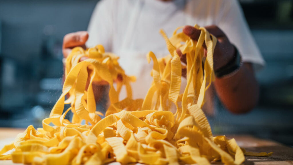 Due mani muovono delle tagliatelle fresche crude appena realizzate