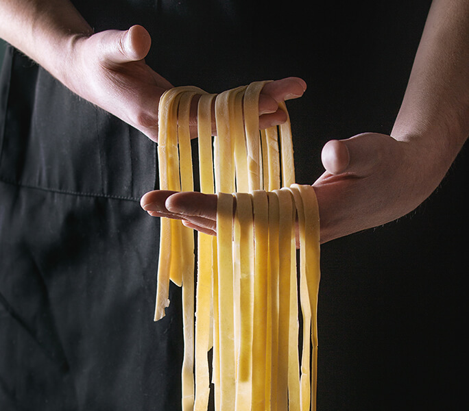 Primo piano di due mani che sorreggono delle tagliatelle fresche crude